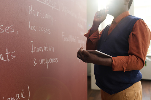 Closeup of senior African American college professor writing on chalkboard while preparing for lecture in college