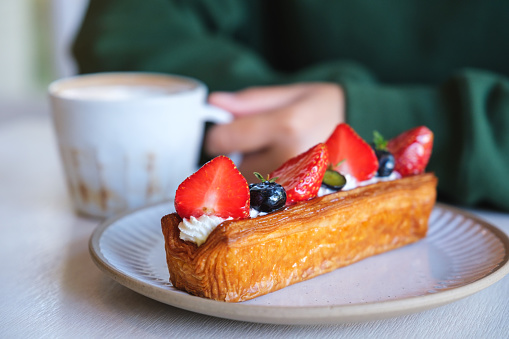 Closeup image of a woman drinking coffee with a plate of mix berry log croissant on the table