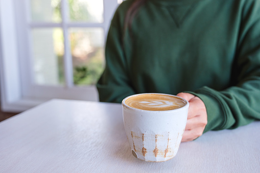 Closeup image of a woman holding a cup of latte coffee