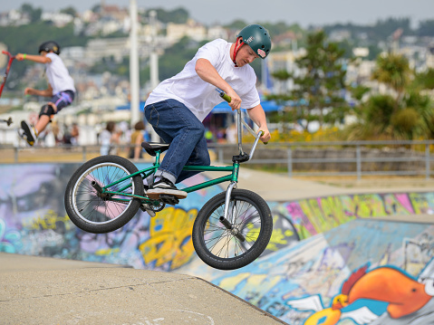 Le Havre, France - July 23, 2022: Young people practicing at a skater park on a cloudy day in summer, boy jumping with bike