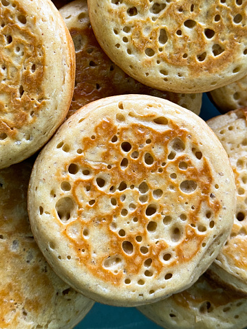 Stock photo showing an elevated view of a turquoise blue, plate containing a pile of freshly baked, warm, homemade crumpets.