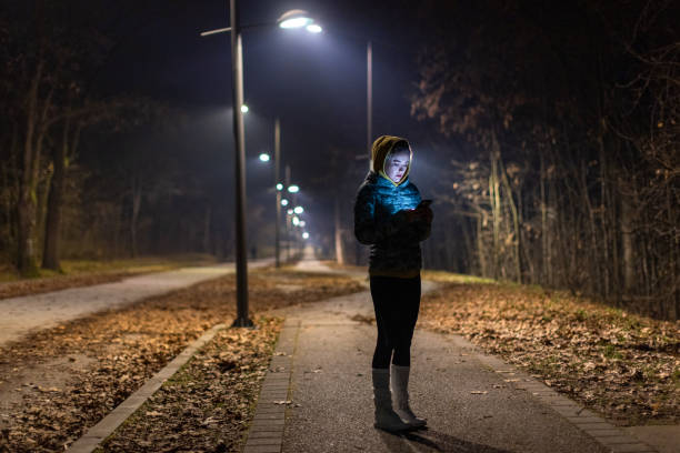 istock Young woman using phone in a park at night 1980048715