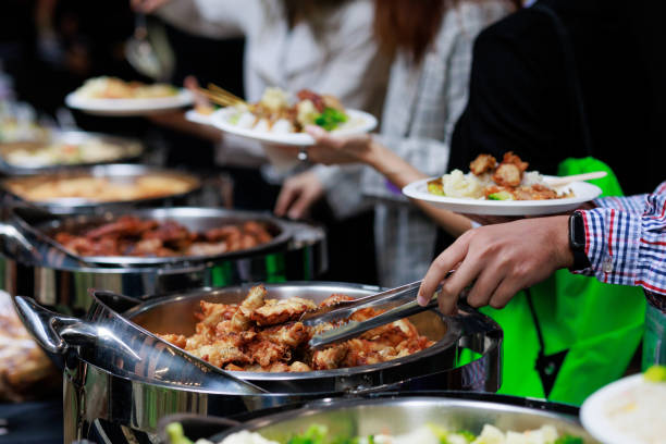 A cropped image captures business people using service tongs to carefully select their food from the buffet line.