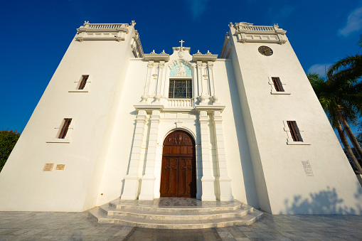 Captured on a radiant sunny afternoon, this image showcases the magnificent exterior of the Inmaculada Concepción Church in Barranquilla, Colombia. The church, a historical and religious landmark, stands proudly under the expansive blue skies. Its gothic-style architecture is highlighted by the ornate facade, intricate stonework, and the presence of stunning stained glass windows that add a colorful vibrancy. The architectural symmetry is evident, with each arch and column meticulously designed, reflecting the church's grandeur and elegance.