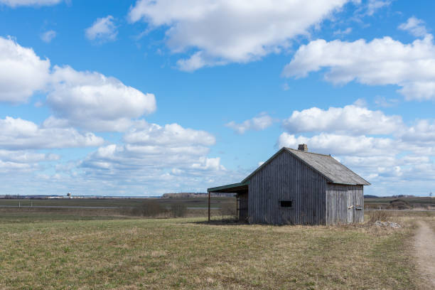 An old abandoned small wooden house in the fields sky clouds, next to a path barn or scary concept.