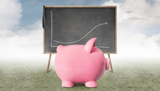 Piggy bank in front of the blackboard, and on the blackboard, there is an economic diagram predicting the future