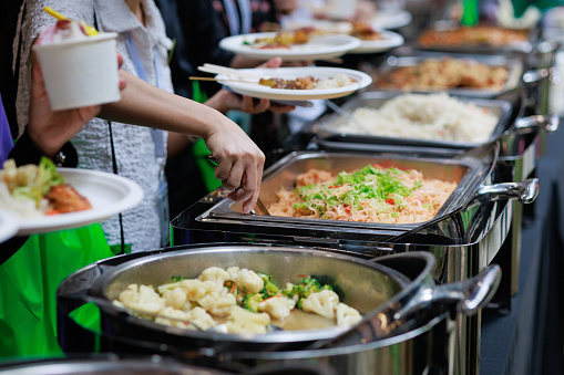 A cropped image captures business people using service tongs to carefully select their food from the buffet line, showcasing a refined and organized dining experience.