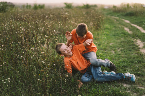 A small group of young children are seen running down a grassy hill with their arms out like airplanes as they enjoy the fresh air.  They are each dressed casually and are laughing and smiling.