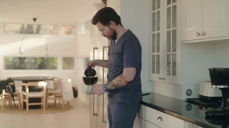 Man wearing medical scrubs pouring a cup of coffee at home