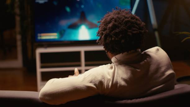 istock Man using cloud gaming service to play demanding science fiction videogame on large TV display 1980133562