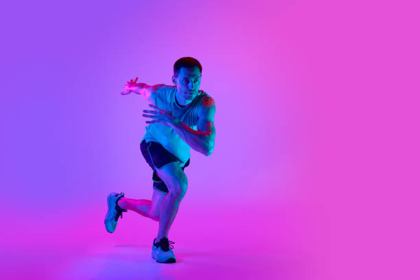 istock Warming-up exercises. Sportive young man in sportswear training, doing exercises against gradient pink background in neon light 1980134622