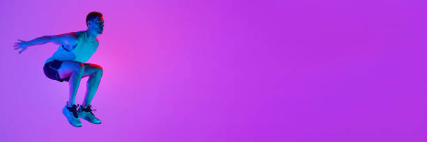 istock Athletic man in sportswear training, jumping against gradient pink background in neon light 1980135130