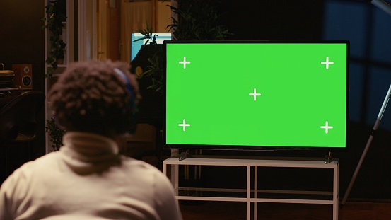 Man playing singleplayer videogames on green screen TV in cozy living room used as home theatre. Gamer using controller to beat game on gaming console attached to mockup television set