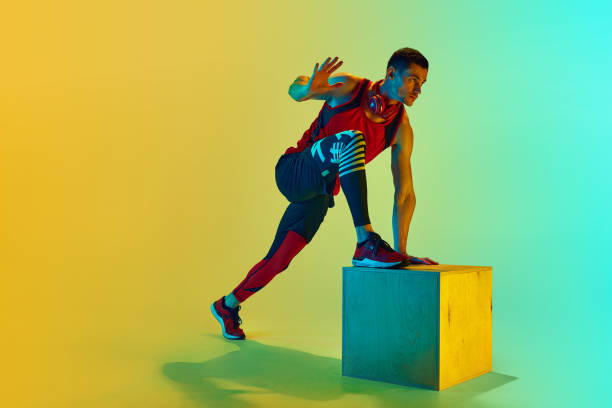 istock Athlete in sportswear training, doing exercises with wooden box against gradient blue yellow background in neon light 1980136732