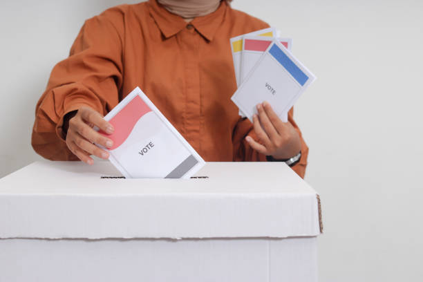 Close up of Asian hijab woman inserting and putting the voting paper into the ballot box. General elections or Pemilu for the president and government of Indonesia. Isolated image on white background stock photo