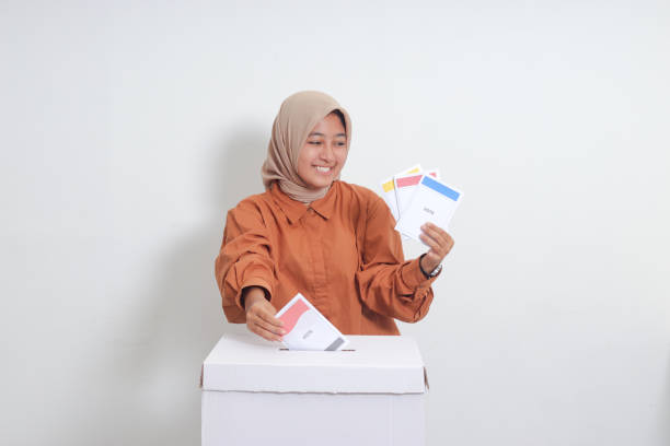 Portrait of Asian hijab woman inserting and putting the voting paper into the ballot box. General elections or Pemilu for the president and government of Indonesia. Isolated image on white background stock photo