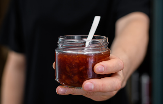 A jar of strawberry jam held in a hand on a black background