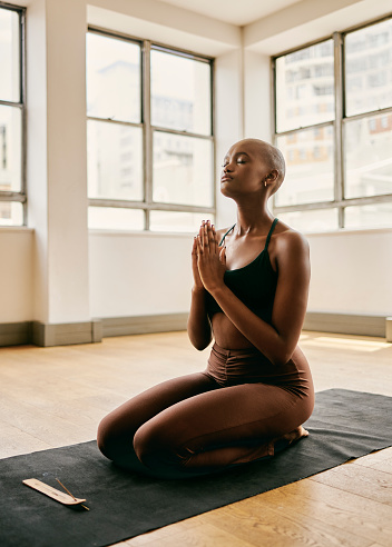 A stock image of a beautiful African woman meditating on a yoga mat in a spacious yoga studio. This image is perfect for any website or marketing campaign focused on wellness and self-care.