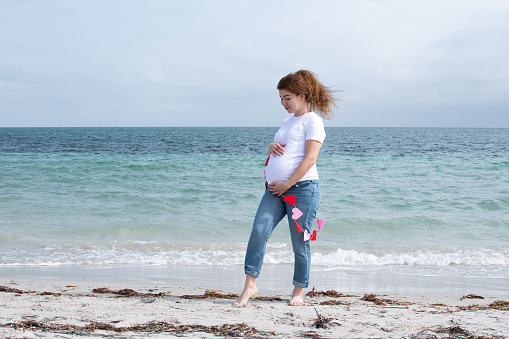 Happy pregnant woman with the string of hearts celebrating Valentine's Day at the beach. Happy pregnancy. Expecting child in Miami. Healthy pregnancy