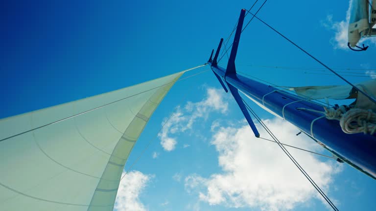 Wind sailboat main mast navigating in open sea. Bright blue sky in the background.