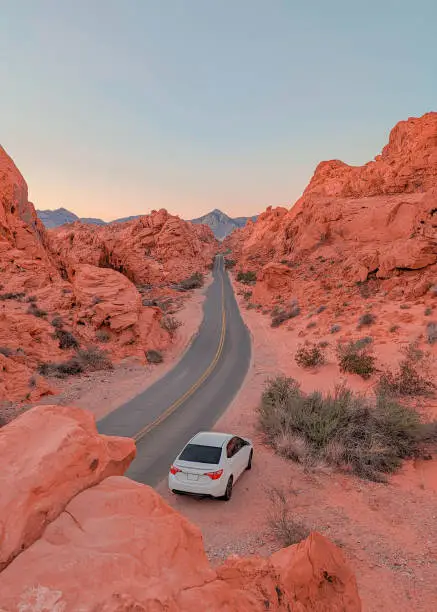 White car parked along Mouse's Tank Road with a view of the mountains and red rocks in Valley of Fire State Park, Nevada.