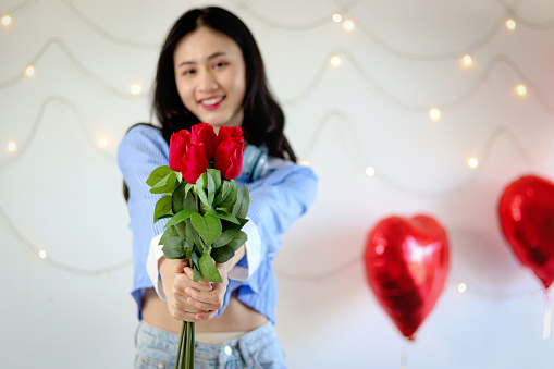 Beautiful red rose bouquet on woman hand, woman holding and showing red rose to camera while standing in decorative room. Romantic girl with flower for celebrating love on Valentine Day.