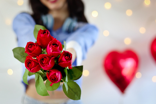 Beautiful red rose bouquet on woman hand, woman holding and showing red rose to camera while standing in decorative room. Romantic girl with flower for celebrating love on Valentine Day.