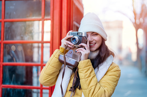 Outdoor portrait of woman using camera against red phonebox in English city