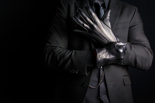 Portrait of Strong Man in Dark Suit Pulling on Black Leather Gloves. Concept of Mafia Hitman or Gentleman Assassin