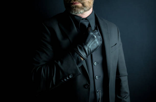 istock Man in Black Suit and Leather Gloves Adjusting Necktie 1980309315