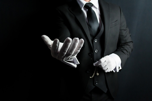 Portrait of Butler or Concierge With Welcoming Gesture in Formal Suit and White Gloves. Service Industry and Professional Courtesy.