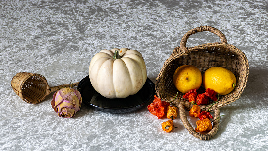 still life on a white tablecloth, fruit in a wicker basket and other objects, black background
