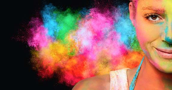 Young woman covered in colored powder with a rainbow color explosion in the background. Festival of colors concept. Panorama banner with copy space.