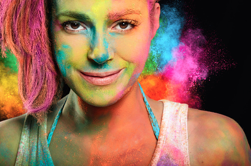 Young woman with holi paints and a rainbow color explosion in the background.