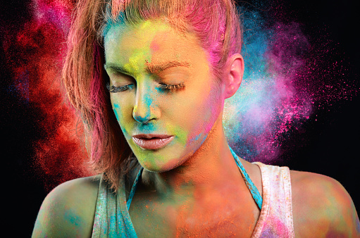 woman covered in colored powder with a rainbow color explosion in the background.
