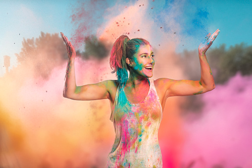 Carefree cheerful woman covered in rainbow colored powder celebrating the festival of colors. Young woman having fun with colorful holi powder