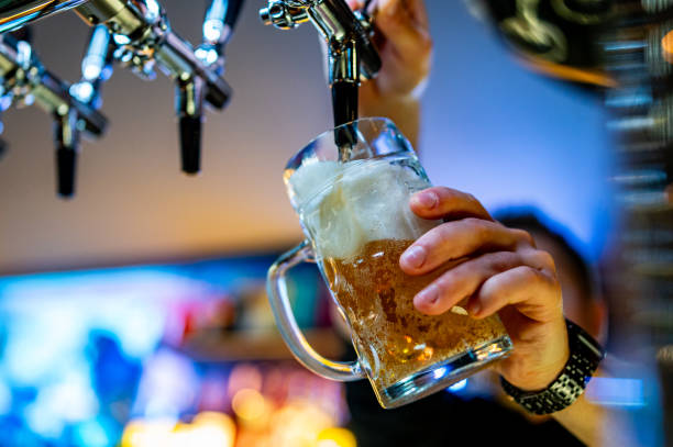 man bartender hand at beer tap pouring beer in glass in bar or pub - Photo