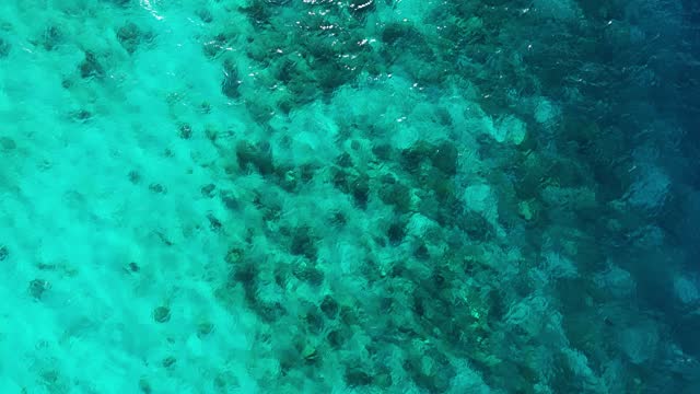 Sandy coral reef drops off to deep open ocean sea, drone descends above water