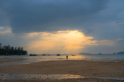 Man in a distance looking at sunset and dramatic sky over the bay of water in Krabi