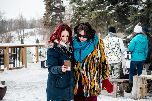 Capturing the essence of friendship and warmth, the non-binary autistic individual and her partner, a woman, snap cheerful selfies with their friends against the backdrop of a crackling winter fire.