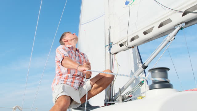 Skilled mature man navigates sailboat using sheet