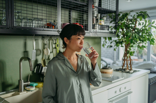 Photo of a Japanese woman drinking a glass of water in her kitchen for a fresh start of the day.