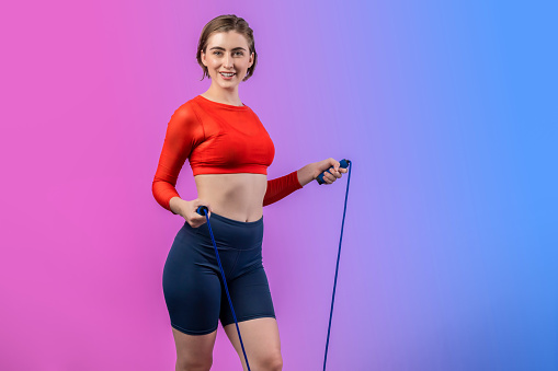 Full body length gaiety shot athletic and sporty young woman with fitness skipping rope in standing posture on isolated background. Healthy active and body care lifestyle.