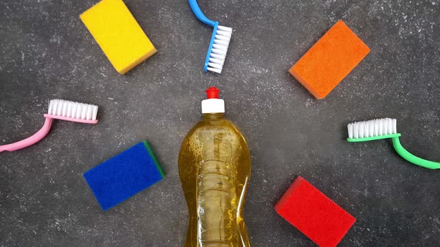 Kitchen sponges, dish brushes and cleaning liquid in bottle appear on dark background.