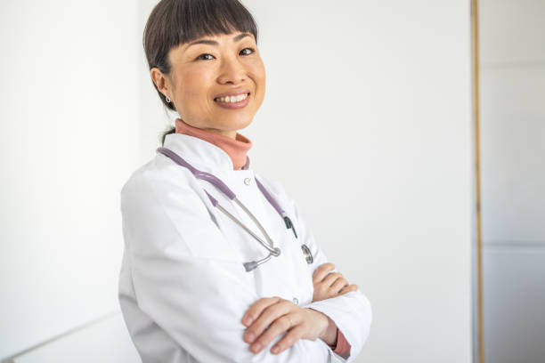 istock Confident female doctor standing by a white wall and gelding into the camera 1980590364