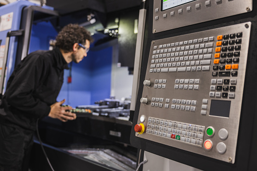 A focused view of a complex control panel of metalworking CNC milling machine, with an engineer meticulously working on machinery. Industrial work concept.