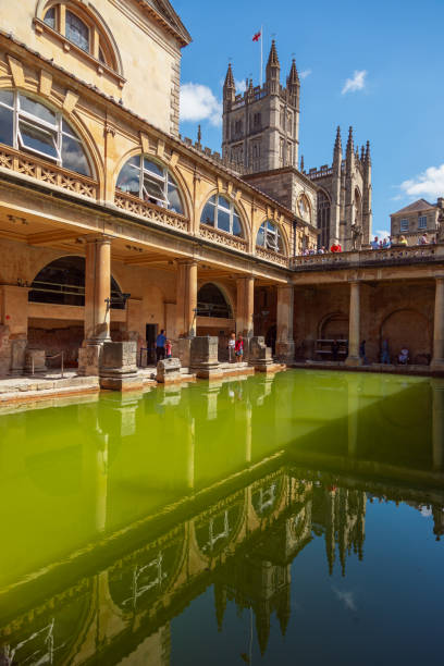 Tourists immerse themselves in history as they visit the iconic Roman Baths inner pool, a captivating glimpse into the ancient past in the charming city of Bath, United Kingdom. A popular landmark, the serene waters mirror the architectural grandeur, inviting visitors to experience the timeless allure of this historical gem