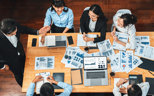 Wide top view of diverse group of business analyst team analyzing financial data report paper on meeting table. Chart and graph dashboard by business intelligence analysis. Habiliment