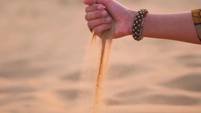 Hand of Indian woman wearing bangles dropping sand at desert in Jaisalmer, Rajasthan, India. Tourist enjoying holidays in desert. Girl playing with fine golden desert sand in sand dunes.