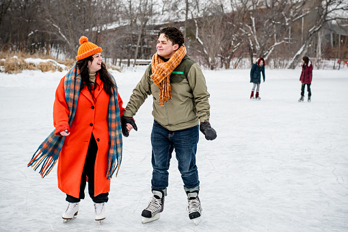 In harmonious motion, the gender fluid individual and trans man skate hand in hand towards the camera, a scene of togetherness against the backdrop of the winter wonderland